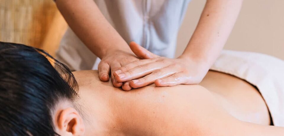 friccion-palmar-espalda-natalia-huba Unas manos con aceite deslizan las palmas una sobre otra en la zona del omóplato de una persona con el cabello oscuro.