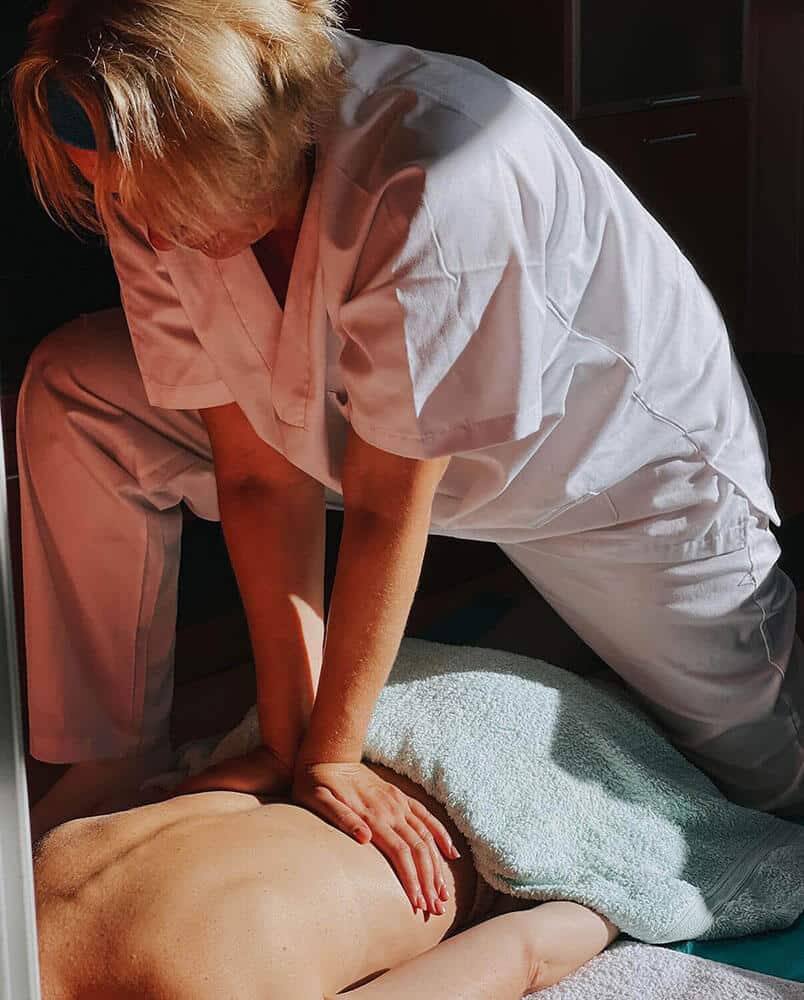 Terapeuta aplicando presión con las palmas de las manos en la espalda de un paciente, utilizando el peso corporal para un masaje profundo y relajante.